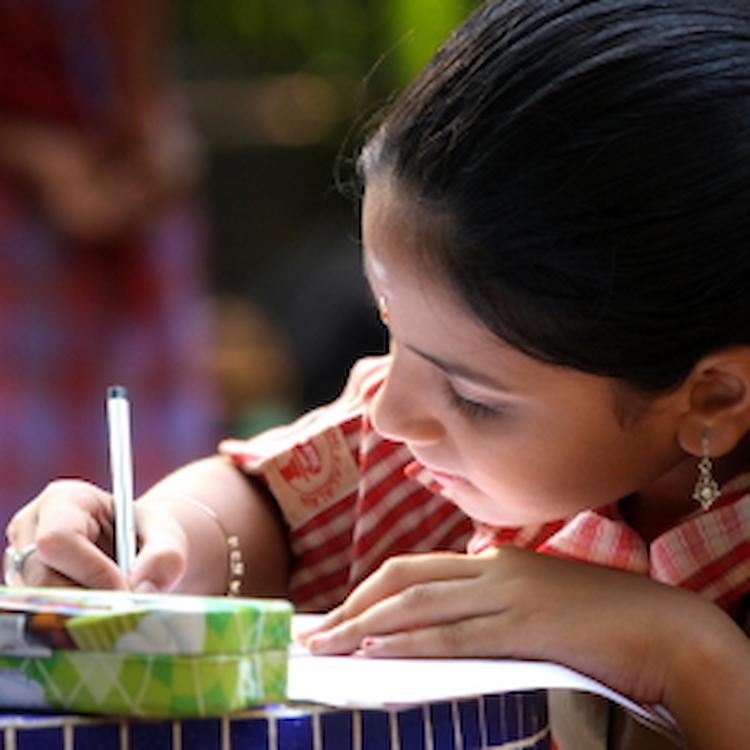 A girl writing in her notebook, focused and engaged in her work, sitting at a desk in a classroom setting.