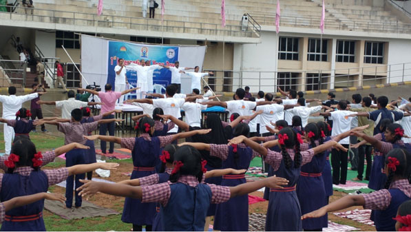 Students gathered in a school assembly, standing in organized rows, listening attentively, with teachers and the school environment in the background.