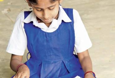 A girl attentively looking at her textbook, focused on reading and learning in a classroom setting.