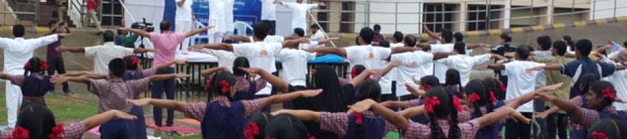 Students gathered in a school assembly, standing in organized rows, listening attentively, with teachers and the school environment in the background.